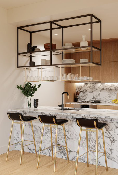 Modern kitchen with marble counters and back splash, light wood cabinetry, matte black faucet and hanging shelf with vases, glasses and dishes and black and gold barstools on light wood floor